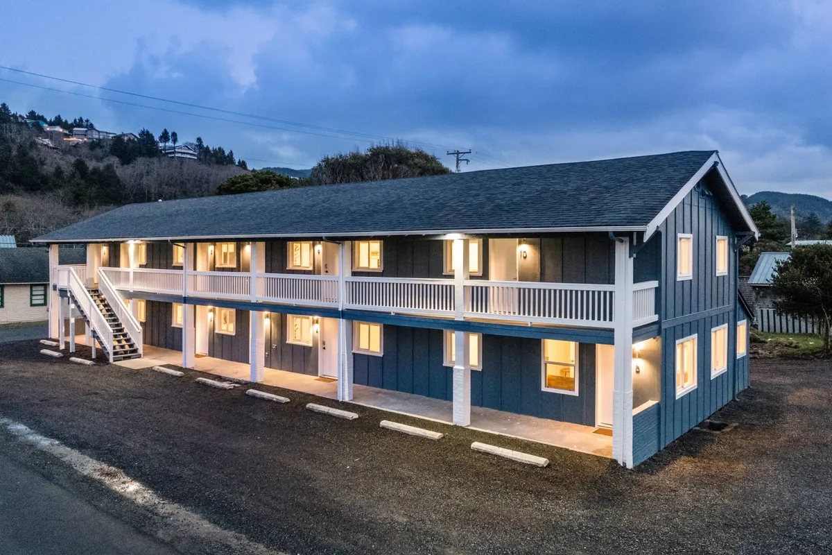 This exterior shot showcases The Inn during the evening, with warmly lit windows and a staircase leading to the second floor. The visible outdoor space hints at communal areas where guests might socialize or relax together, reflecting the lively energy of the community.
