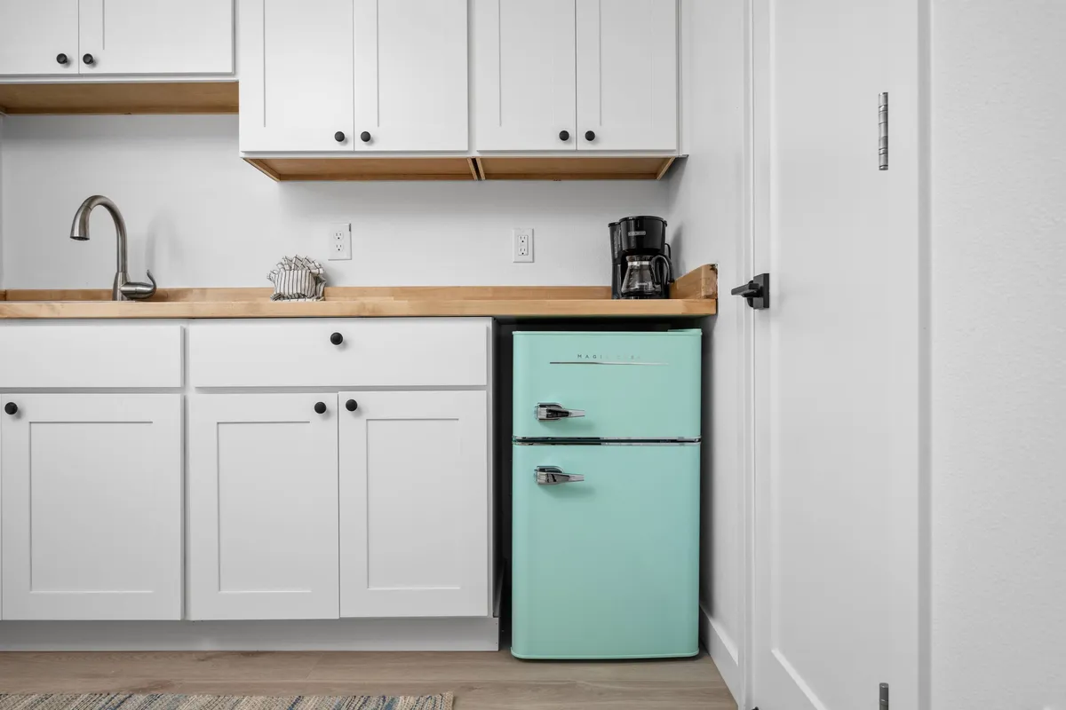 A cheerful, compact kitchenette space with a mint green refrigerator, wooden countertop, and coffee maker. The area looks fresh and inviting, ideal for preparing light snacks, morning coffee, or quick meals, and encourages a sense of ease and practicality.